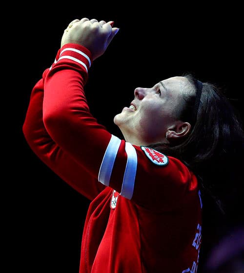 Female Canadian Olympic athlete holding medal up in the air with both hands.