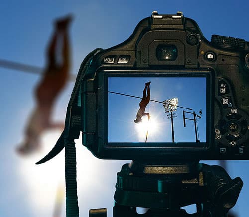 A professional camera on a tripod captures a high jump performance