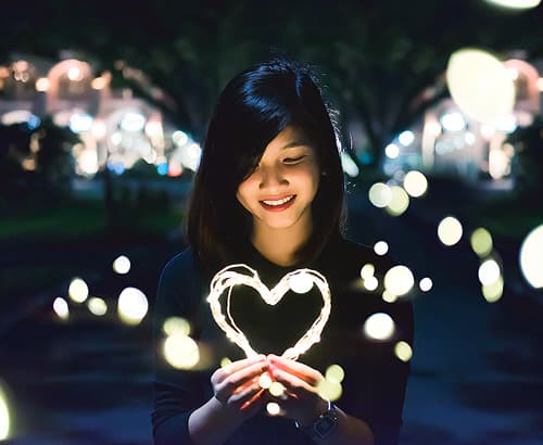 custom content - Young woman playing with lights shaped like a heart.