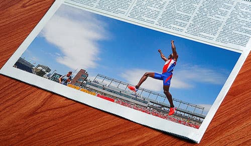 Newspaper image of a track and field athlete jumping in mid-air in an outdoor stadium.