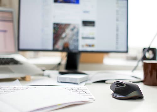 A desk furnished with a keyboard, monitor, pen, and writing paper.