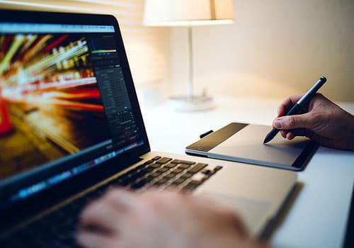 Video editing software displayed on a laptop and person making notes.