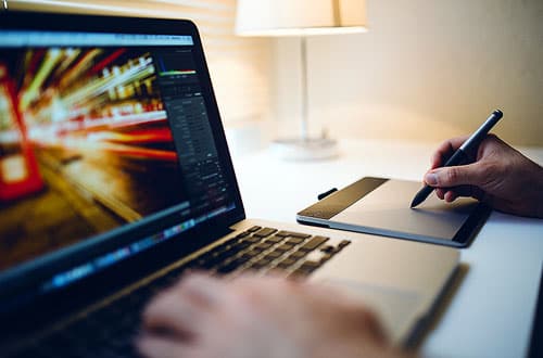 Video editing software displayed on a laptop and a person making notes.