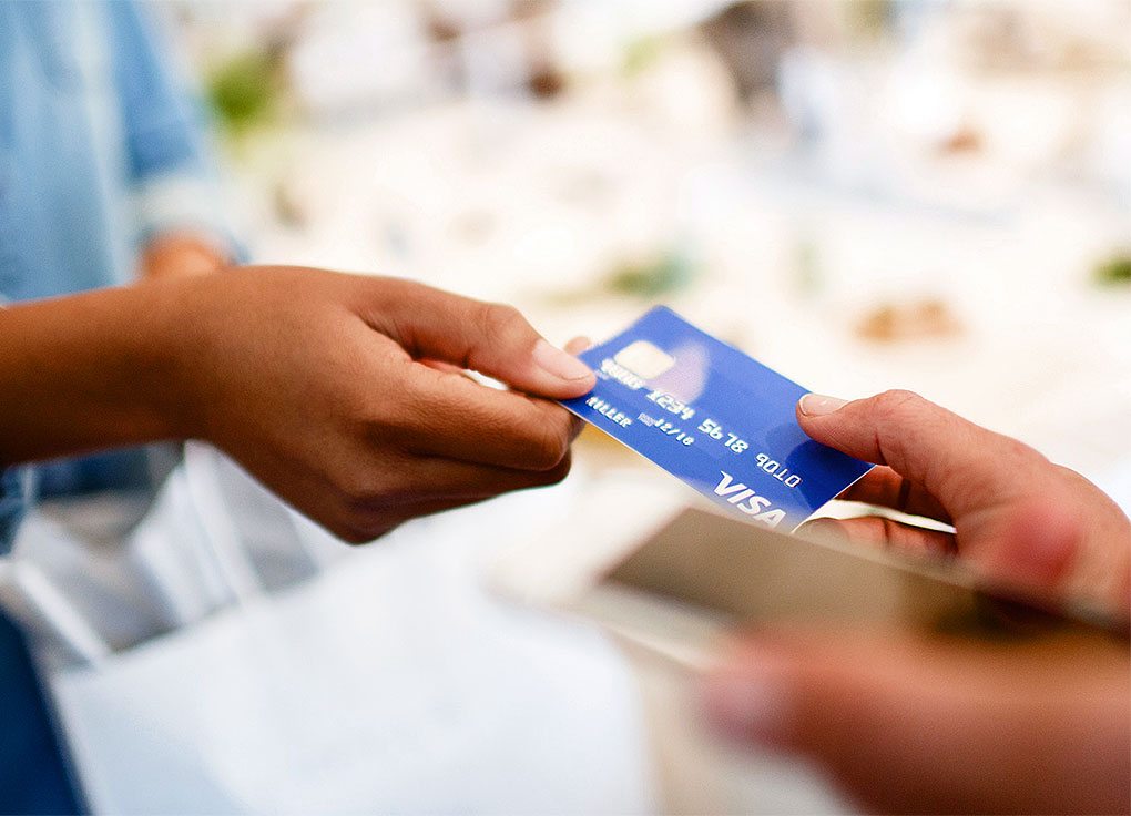 A person handing a Visa card to another person.