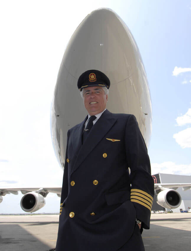 Picture of a commercial pilot in uniform standing under a plane.