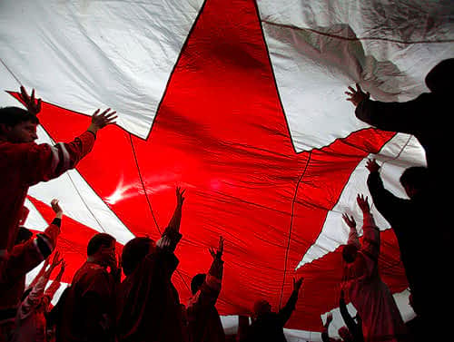 Group of people standing under a large parachute with a red maple leaf emblazoned on it.