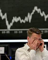 Man standing in front of a stock market screen.