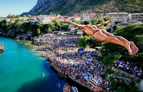 A man diving in a lake with people in boats and on the beach spectating.