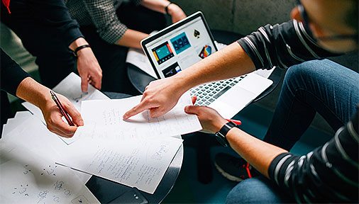 Three people gathered around a laptop and papers planning.