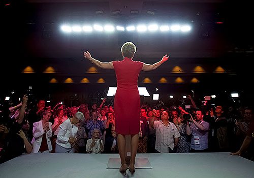 A picture of Kathleen Wynne from behind, standing on a stage, speaking to a group of people.