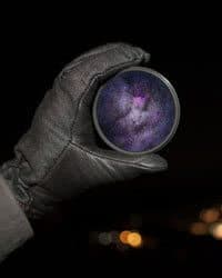 Hand holding a circular glass to the night sky, magnifying the galaxy.