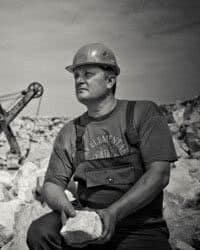 A man wearing a hard hat, sitting in a rock quarry.