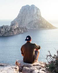 Man sitting on the edge of a cliff looking out into the ocean landscape.