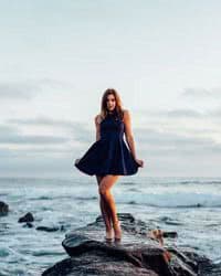 A female model posing in a black dress on the beach.