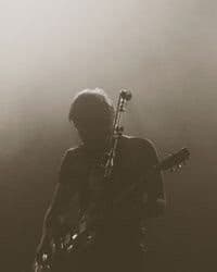 Silhouette of a guitarist standing next to a mic on a stage.