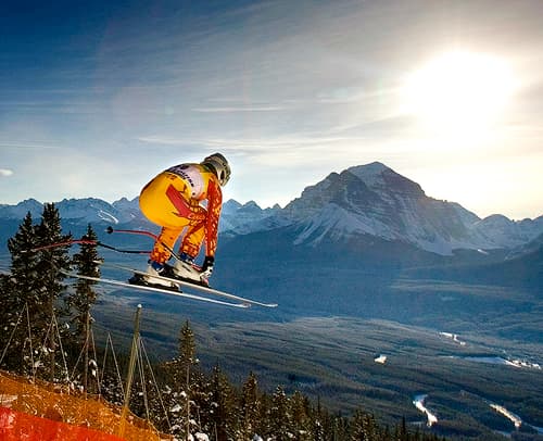 Olympic skier pictured jumping in mid-air with a mountain in the distant background.