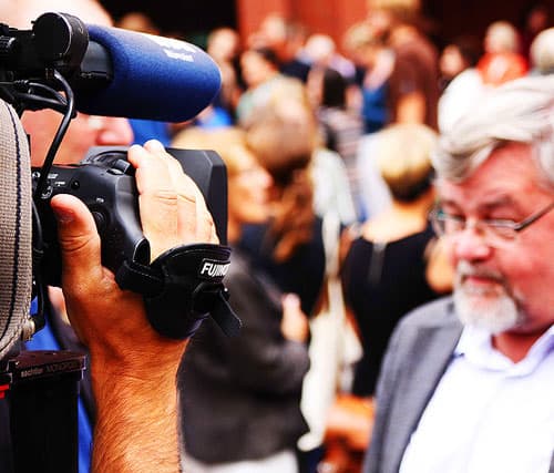 Grey haired man with glasses being filmed