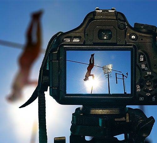 A professional camera on a tripod captures a high jump performance