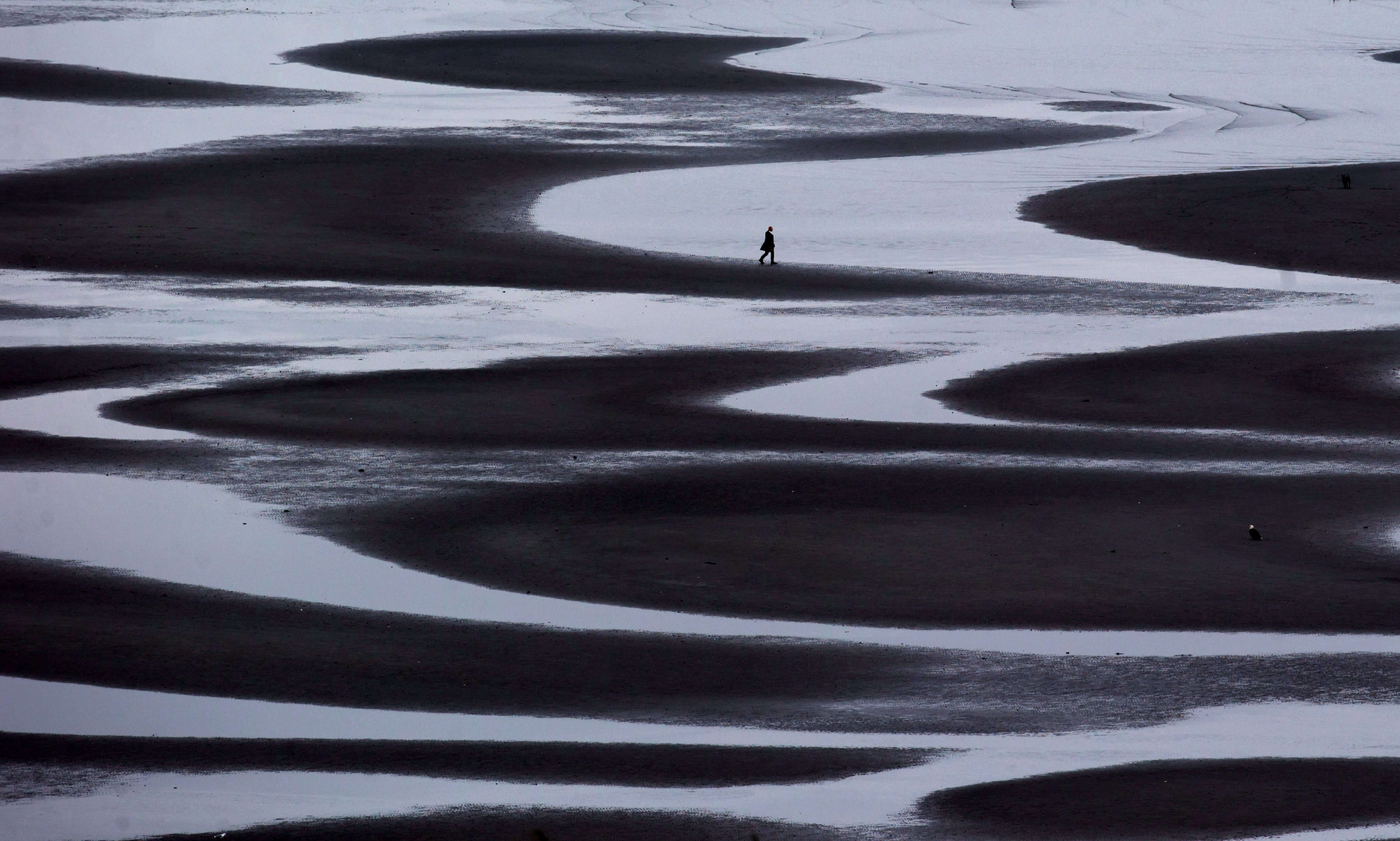 A woman walking through a tidal pool along the shore of Semiahmoo Bay during low tide in White Rock, British Columbia.