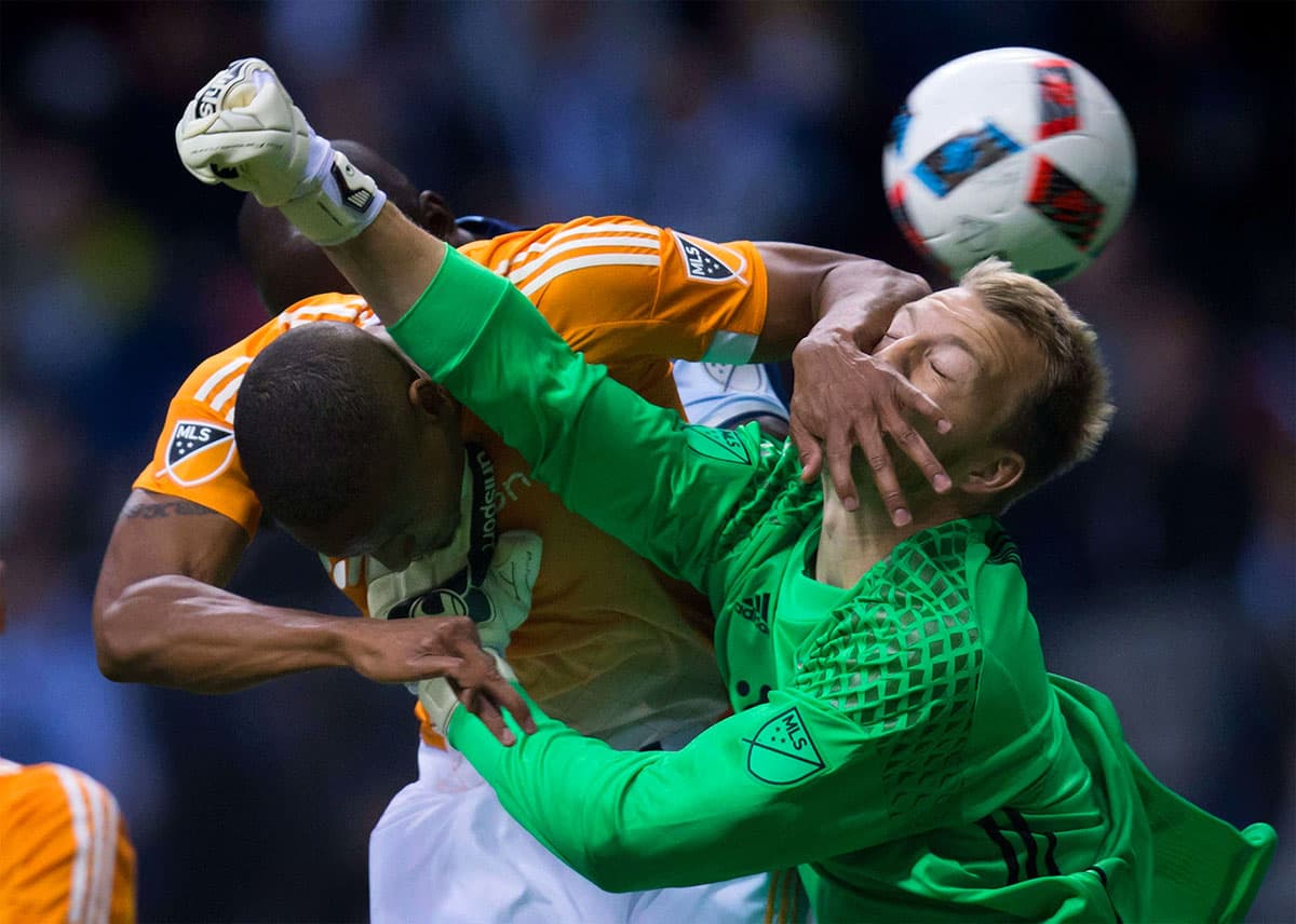 Dynamo's Ricardo Clark gets his hand in the face of teammate, goalkeeper Joe Willis, as he tries to punch the ball away from Vancouver Whitecaps' Kekuta Manneh.