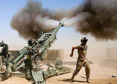 Cannon being fired by soldiers in a desert.