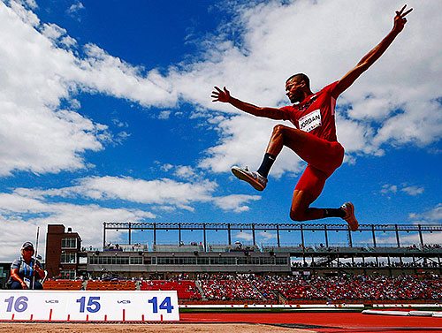 Track and Field athlete pictured mid-air during long jump event.