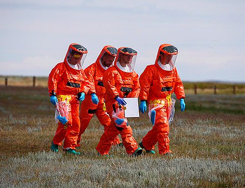 Four people walking in a field wearing hazmat suits.