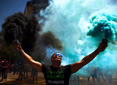 A muscular man holding two smoke grenades, one issuing black smoke and the other issuing blue smoke.