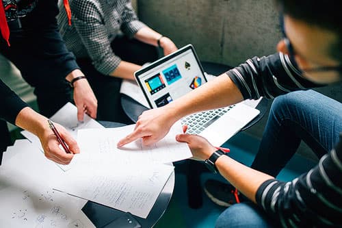 Three people gathered around a laptop and papers planning.