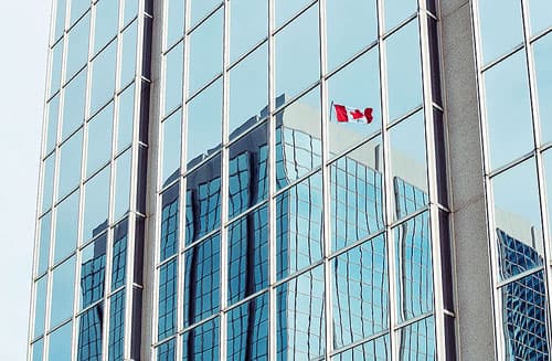 A Canadian Flag reflected in the modern glass of a business tower