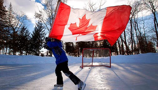 A boy skating on a frozen pond with a Canadian flag tied to a hockey stick