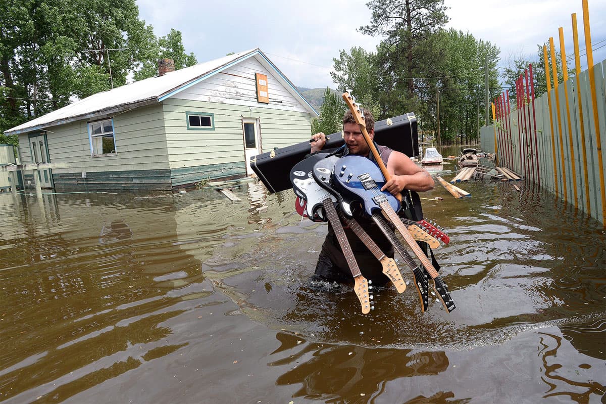 Lars Androsoff carries his friend's guitars as he walks through the floodwaters in Grand Forks, B.C.