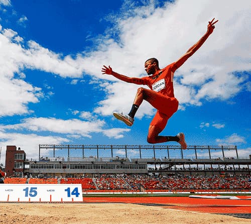 Track and Field athlete pictured mid-air during long jump event.