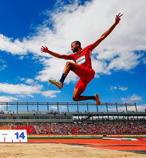Track and Field athlete pictured mid-air during long jump event.