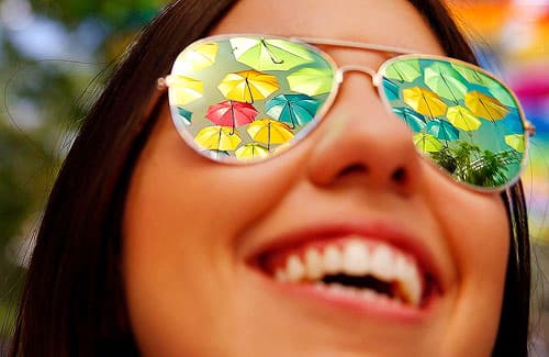 Umbrellas reflected in a gleeful woman's sunglasses