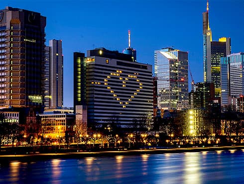 FOR HOLD ———File - In this Sunday, March 22, 2020 file photo, a hotel has switched on the lights in some rooms to form a heart near the buildings of the banking district in Frankfurt, Germany, as the German government announced new public restrictions to help avoid the spread of Coronavirus. For some people the COVID-19 coronavirus causes mild or moderate symptoms, but for some it can cause severe illness including pneumonia. Germany has hit another grim milestone in the coronavirus pandemic ticking above 1 million confirmed coronavirus cases. The Robert Koch Institute, the country’s disease control center, said that Germany’s 16 states reported 22,806 new cases overnight Friday, Nov. 27, 2020, for a total since the start of the outbreak of 1,006,394. (AP Photo/Michael Probst, file)
