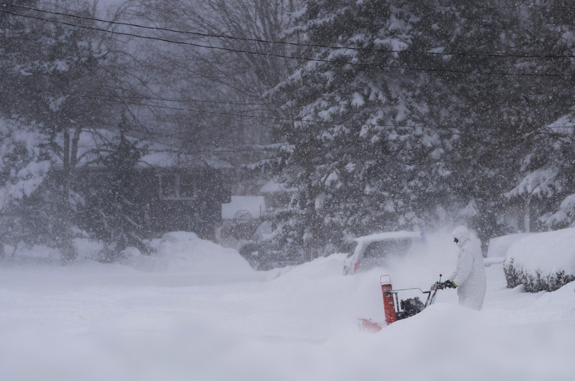 A man all in white uses a snow blowing machine on his driveway