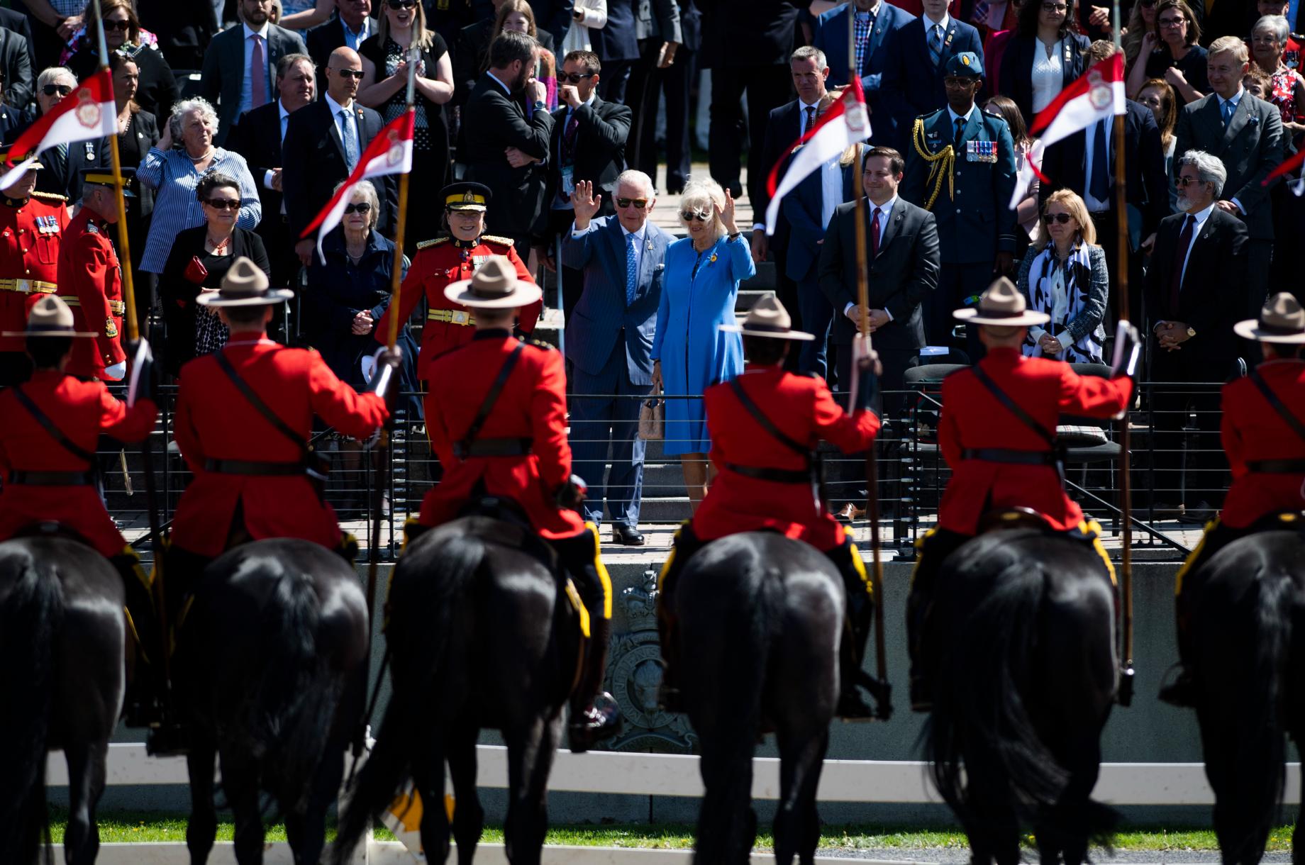 In this wide shot, the backs of mounties on horses are seen while Charles and Camilla face the camera waving.